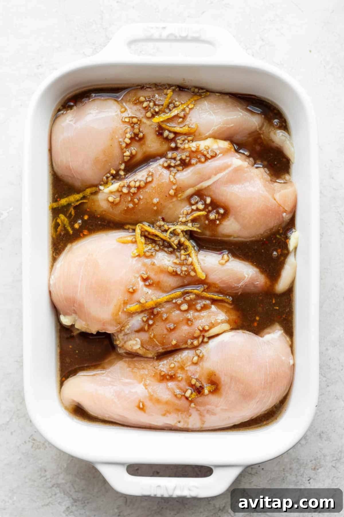Raw chicken breasts fully submerged in marinade within a glass casserole dish.