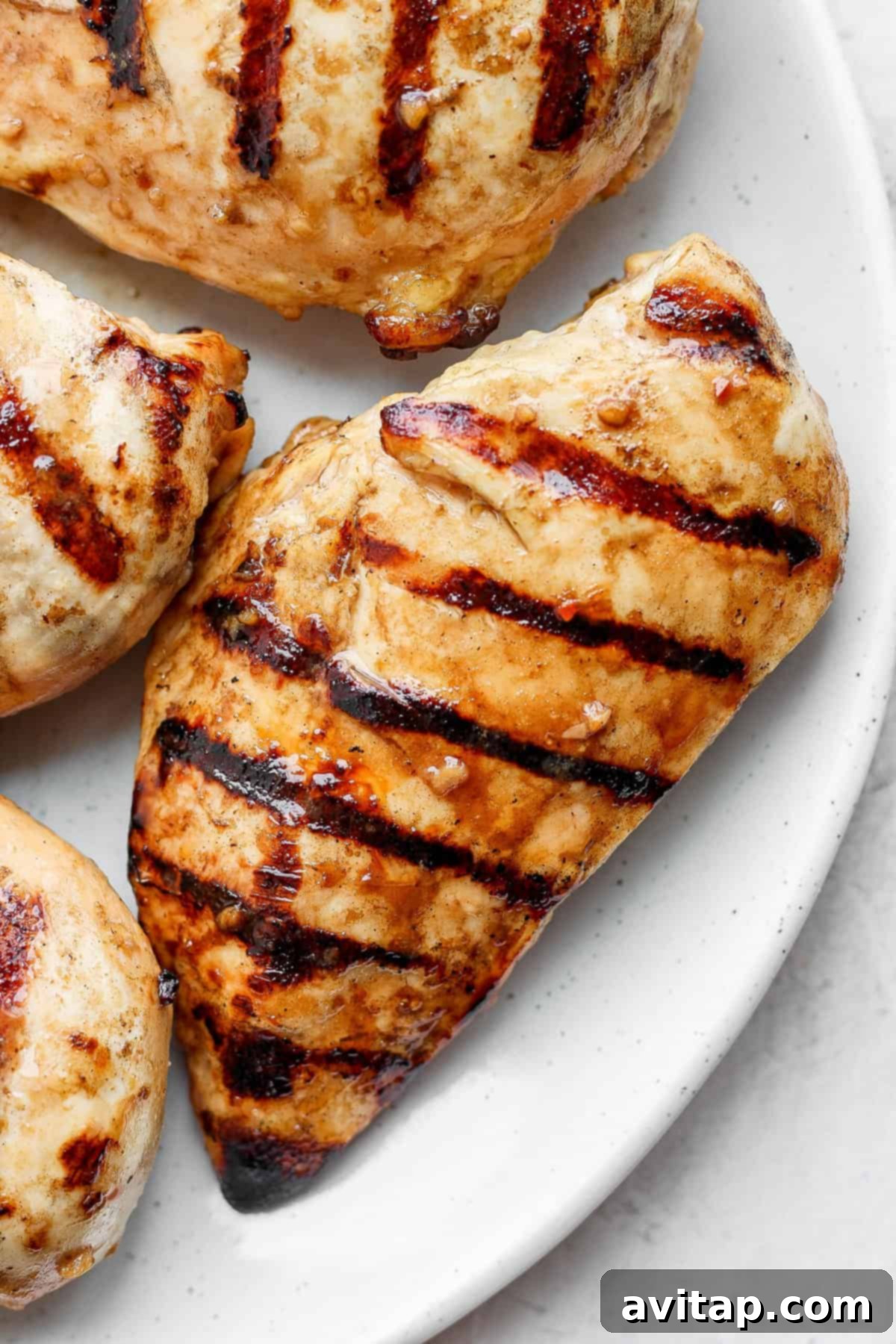 A beautifully grilled chicken breast on a white plate, garnished with fresh herbs.