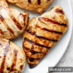 Grilled chicken breasts on a white plate, showcasing its juicy interior.
