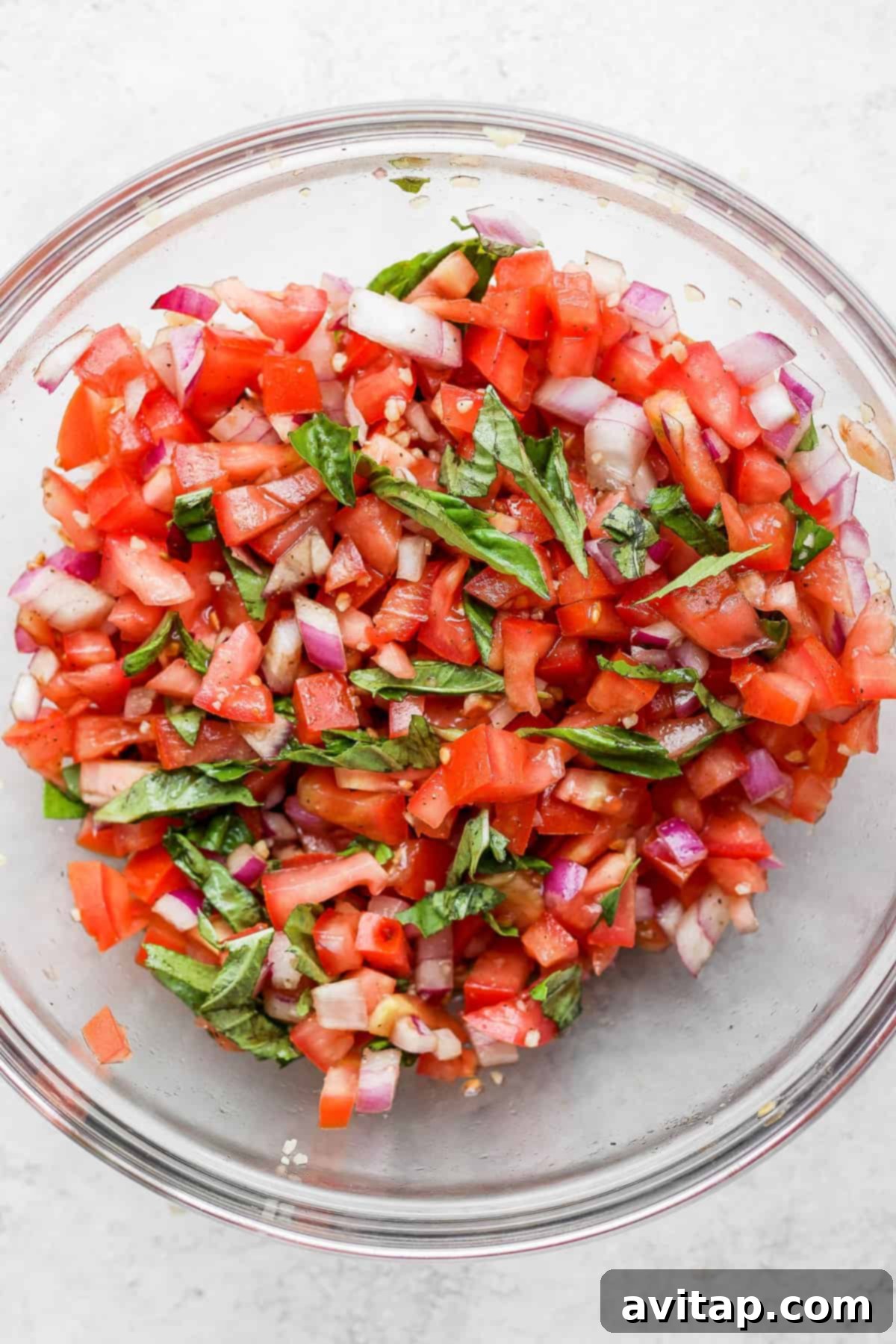 A glistening bowl of fresh bruschetta, bursting with ripe tomatoes and green basil leaves.