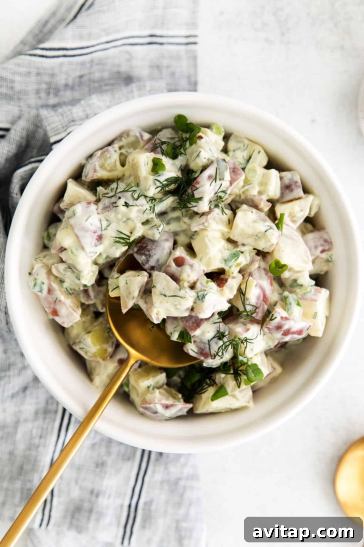 A vibrant bowl of creamy red potato salad, garnished with fresh dill.