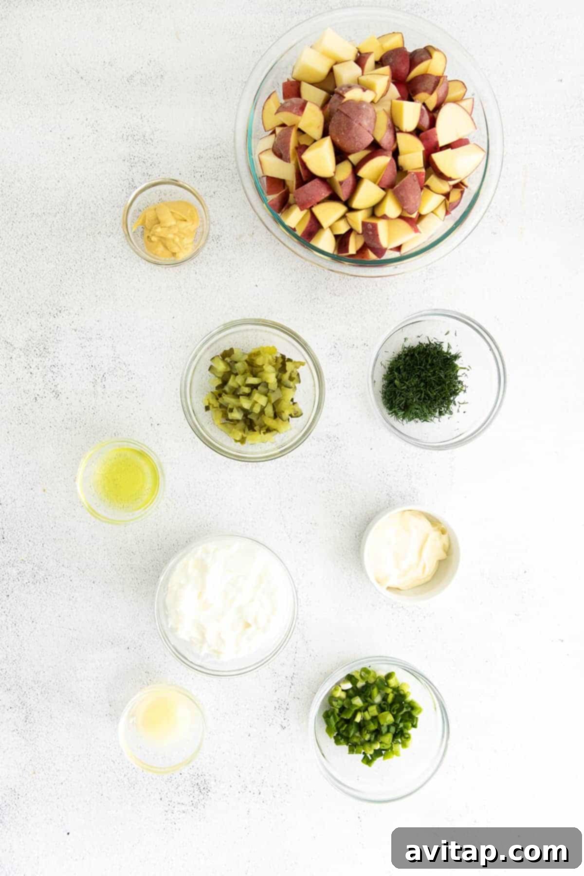 Assortment of fresh ingredients for red potato salad in small bowls, including dill, green onions, and pickles.