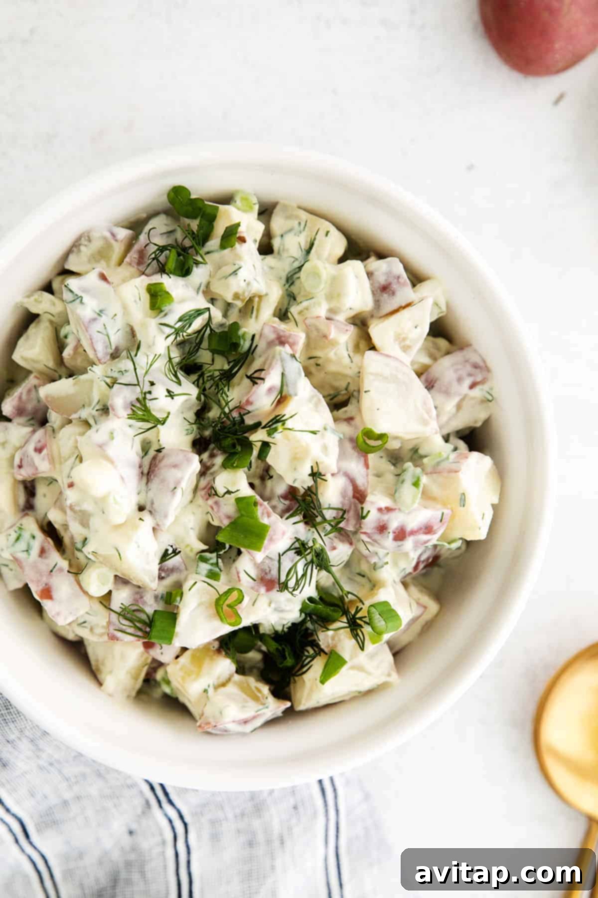 A beautifully presented bowl of creamy red potato salad, garnished with fresh dill.