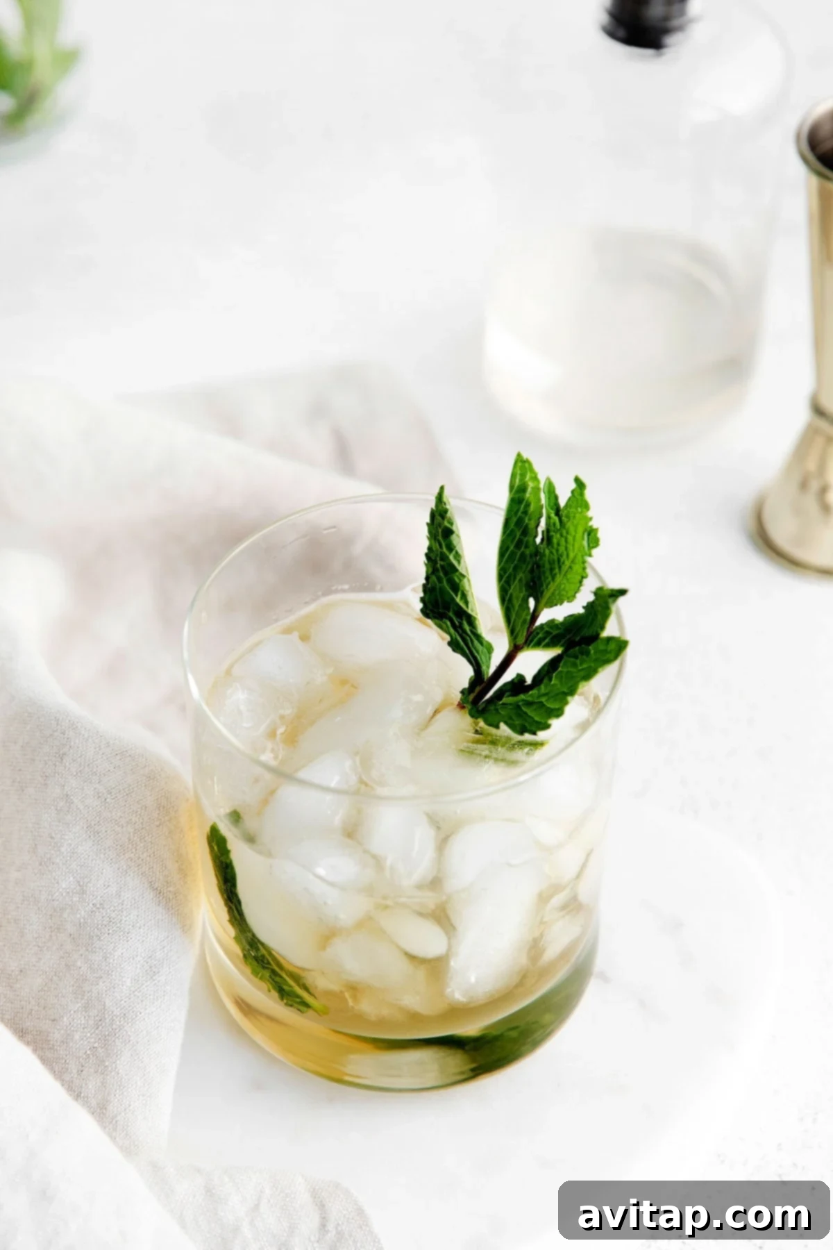 A vibrant Mint Julep cocktail served in a classic Julep cup, garnished with a generous sprig of fresh mint, set against a blurred background.