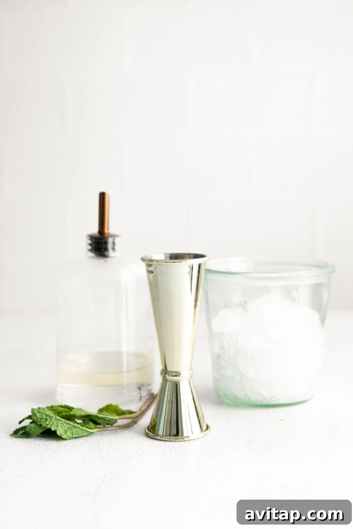 Key ingredients for making a Mint Julep — fresh mint, a bottle of bourbon, and simple syrup — laid out on a surface, ready to be mixed into the cocktail.