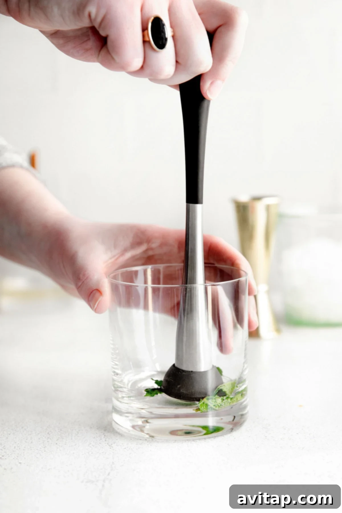 Fresh mint leaves being gently muddled with simple syrup in the bottom of a glass, preparing the base for a Mint Julep.