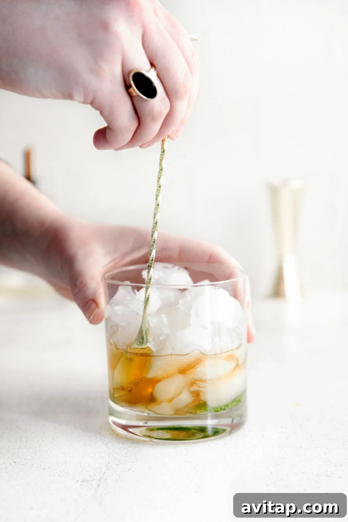 A stream of rich amber bourbon being poured and stirred into a glass filled with crushed ice and muddled mint, the foundational elements for a Mint Julep.