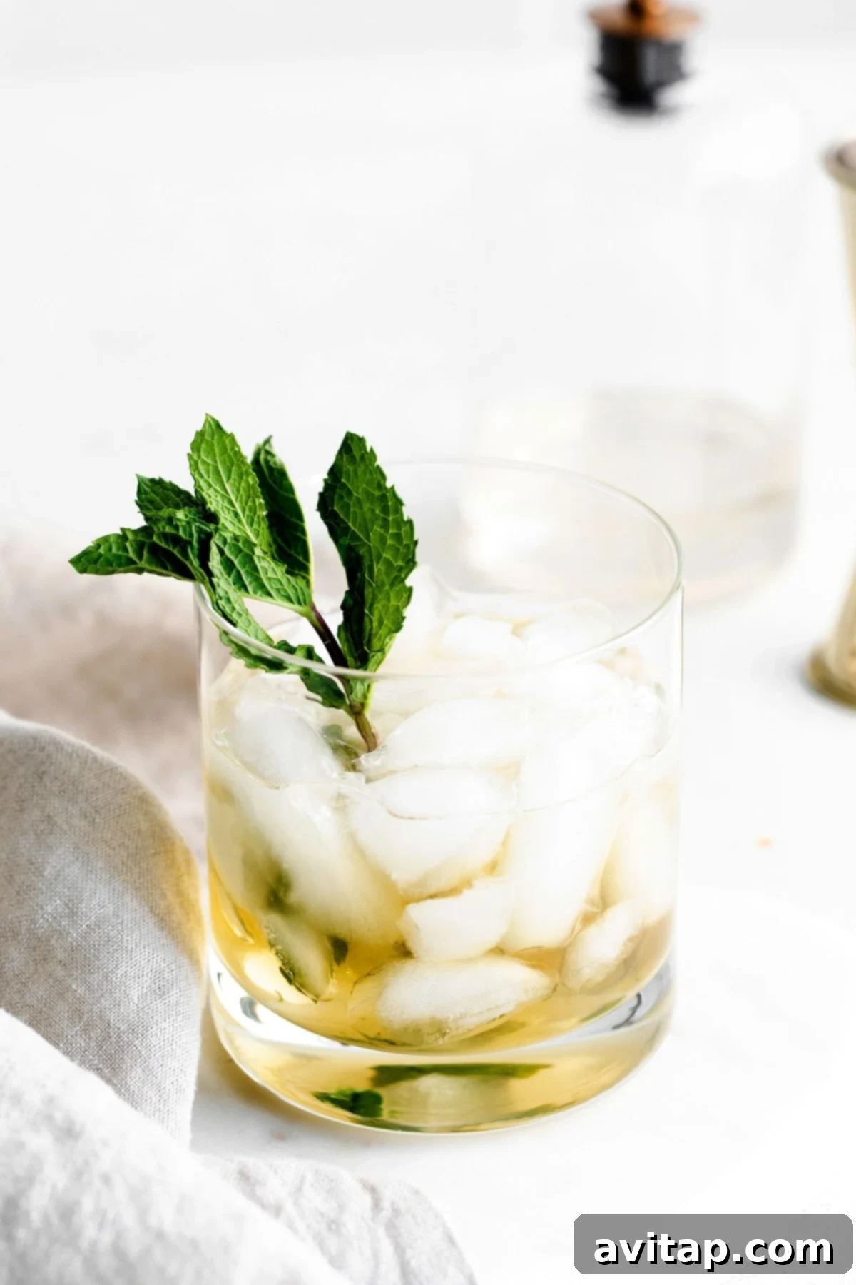 A pristine Mint Julep served in a clear lowball glass, garnished with vibrant fresh mint leaves, highlighting the crushed ice and the rich amber hue of the cocktail.