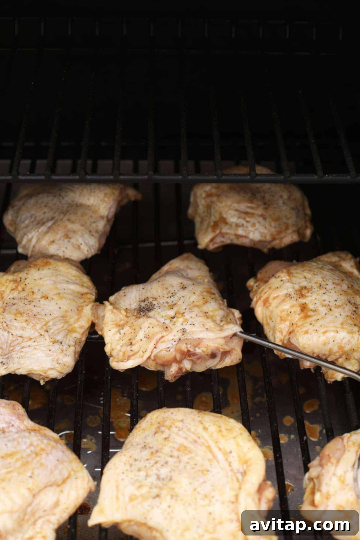 Juicy Smoked Chicken Thighs 6 Several chicken thighs with crispy, golden-brown skin smoking on the grates of an outdoor pellet grill, emitting delicious aroma.
