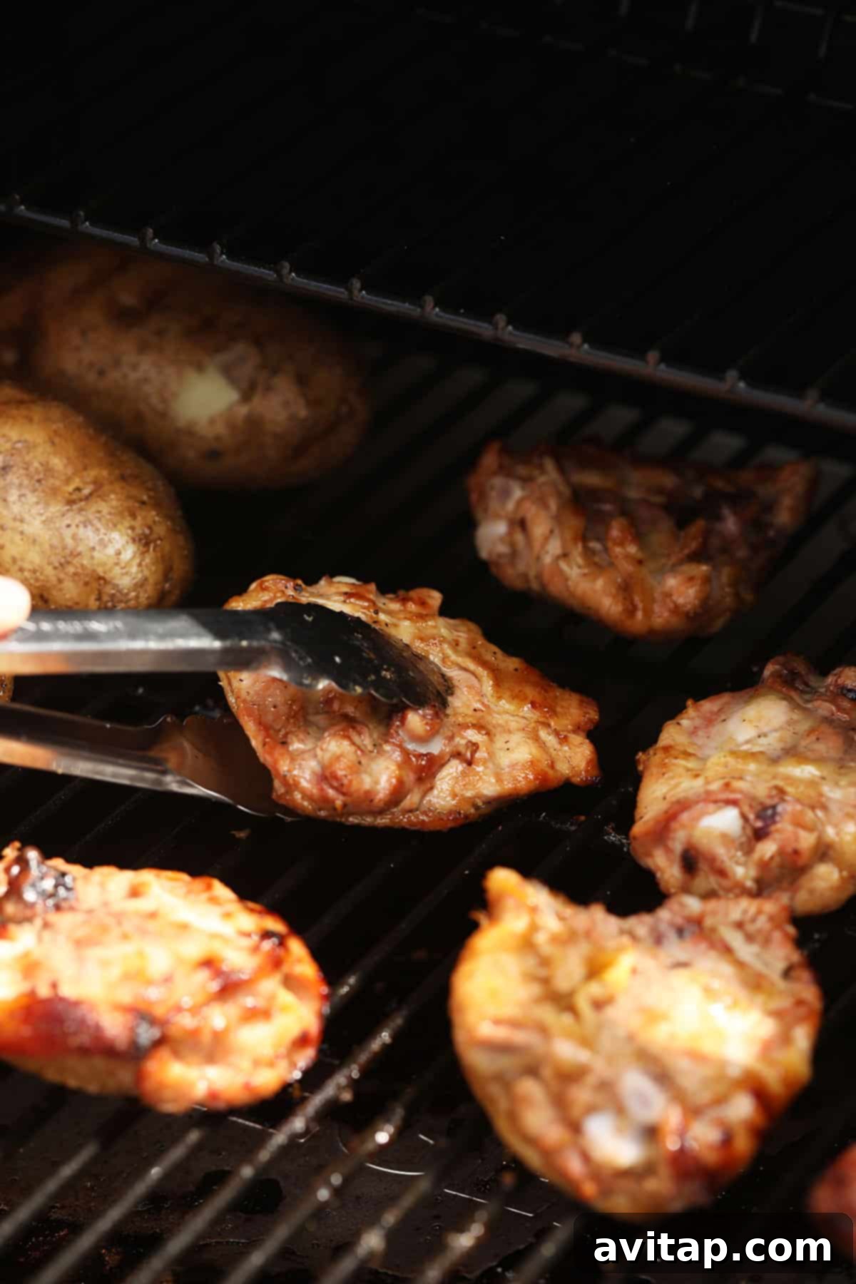 Juicy Smoked Chicken Thighs 7 A hand using tongs to flip chicken thighs on a smoker, revealing perfectly seared skin and juicy meat.