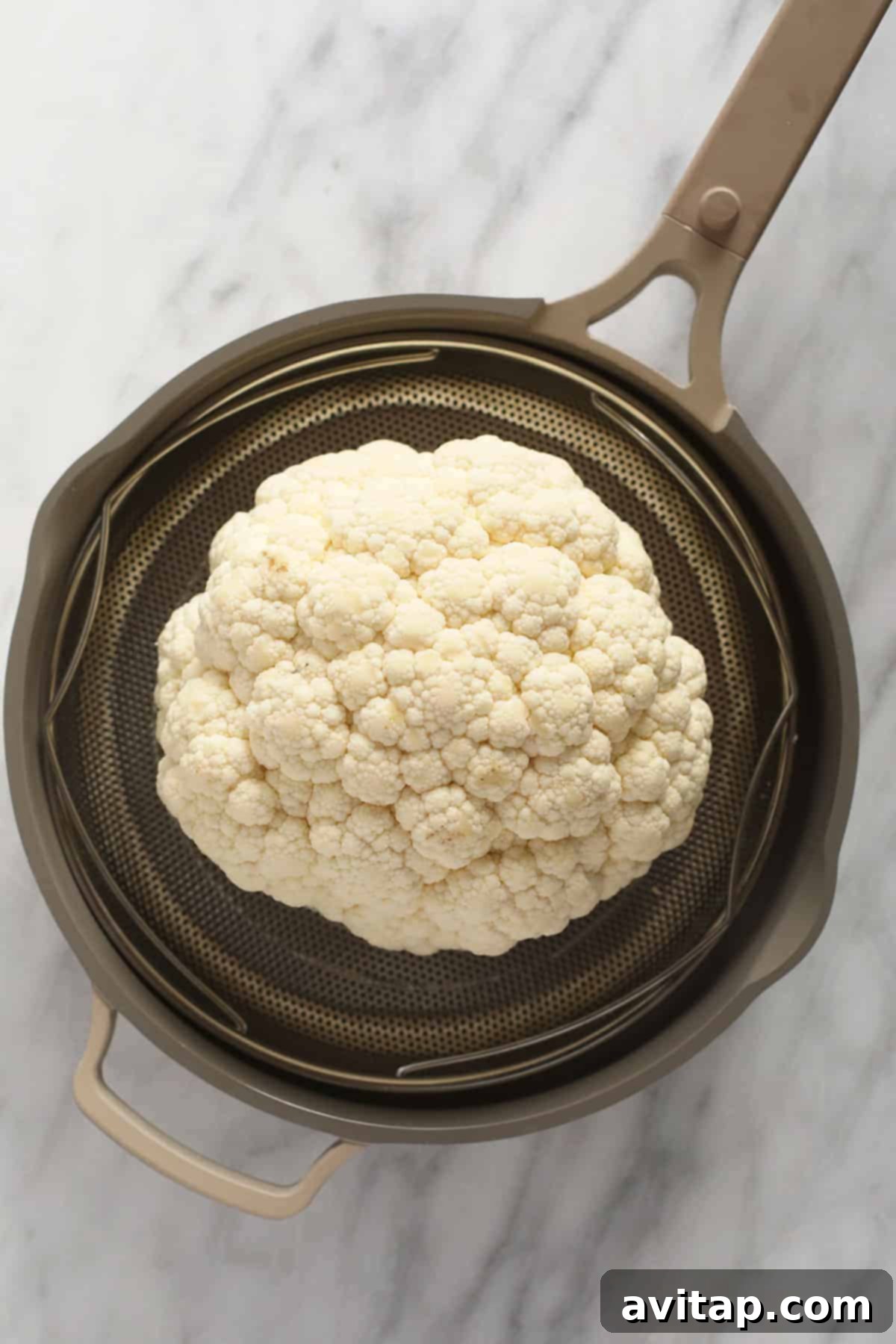 A pristine head of cauliflower placed inside a steaming basket, ready for pre-cooking.