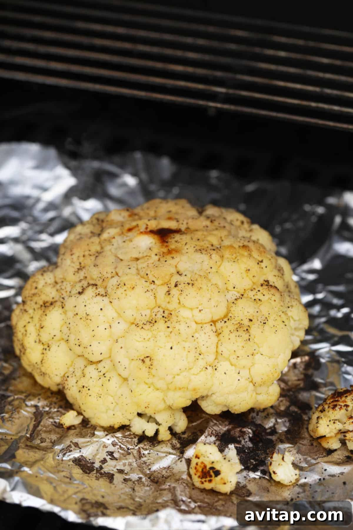A glistening, whole head of seasoned cauliflower resting directly on the hot grill grates, ready to achieve perfect char.