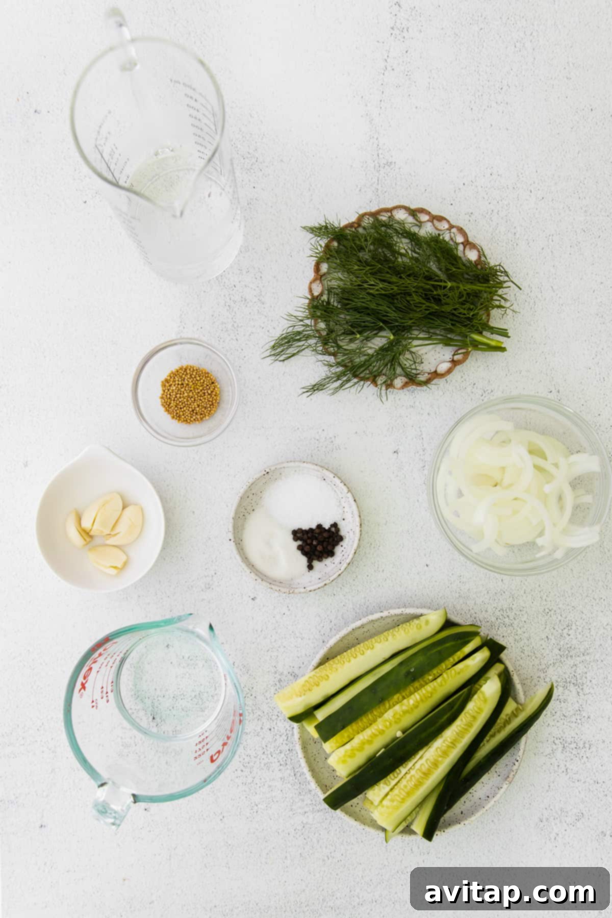 Sliced cucumbers, fresh dill, white onion, mustard seeds, sugar, garlic, and vinegar arranged on a countertop, ready for pickling.