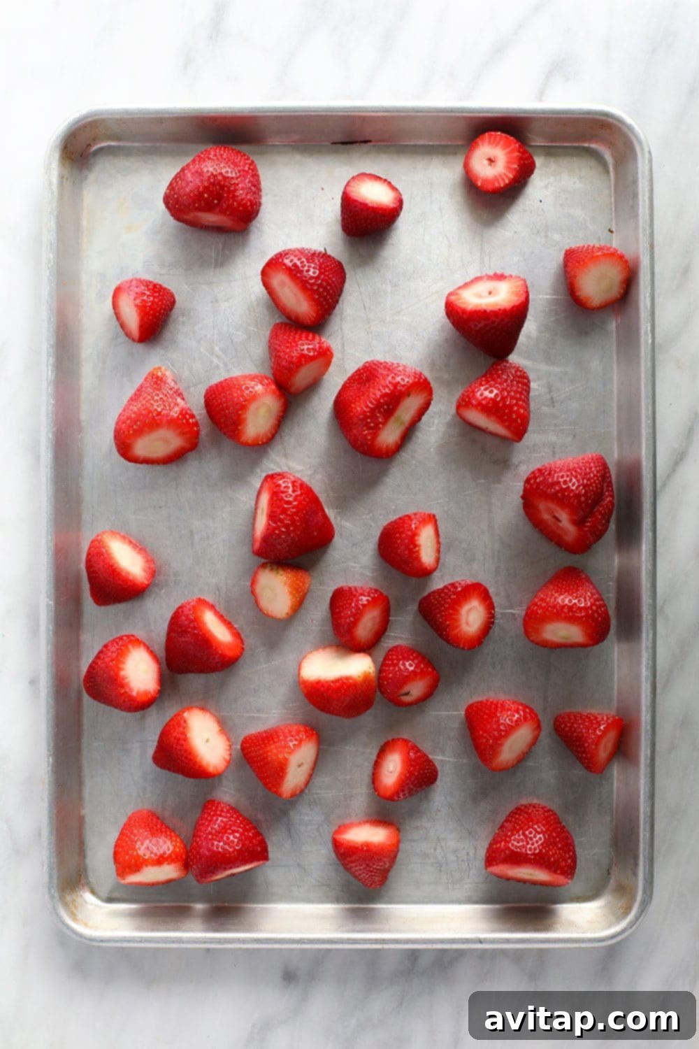 Freshly prepared strawberries spread out evenly in a single layer on a baking sheet, ready for flash freezing.
