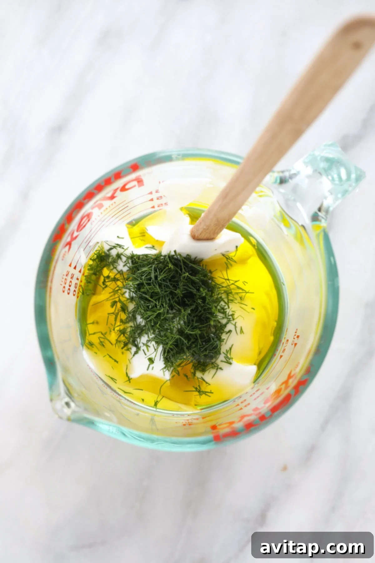 Various Greek yogurt dressing ingredients neatly arranged in small clear glass mixing bowls on a light surface.