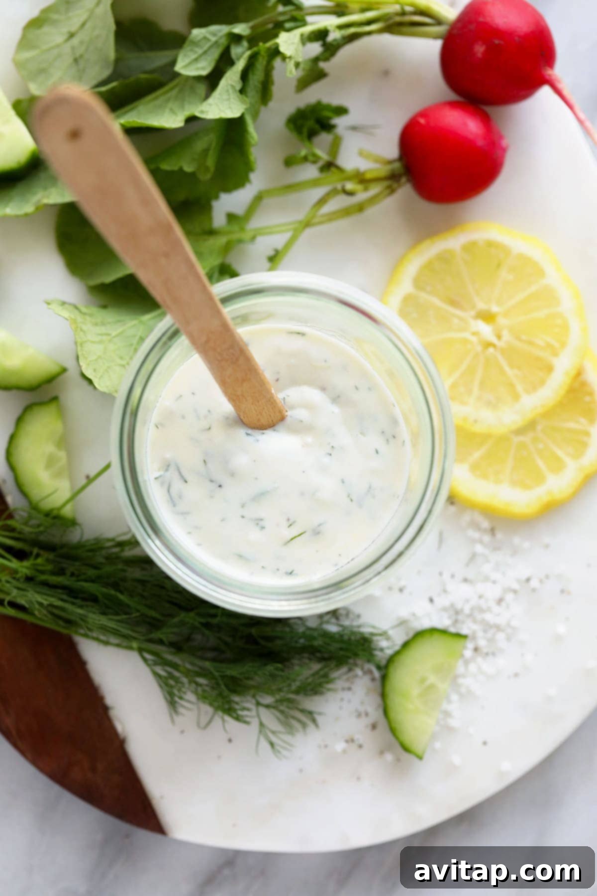 A Mason jar filled with creamy Greek yogurt dressing, featuring a spoon dipped into it and garnished with fresh dill.