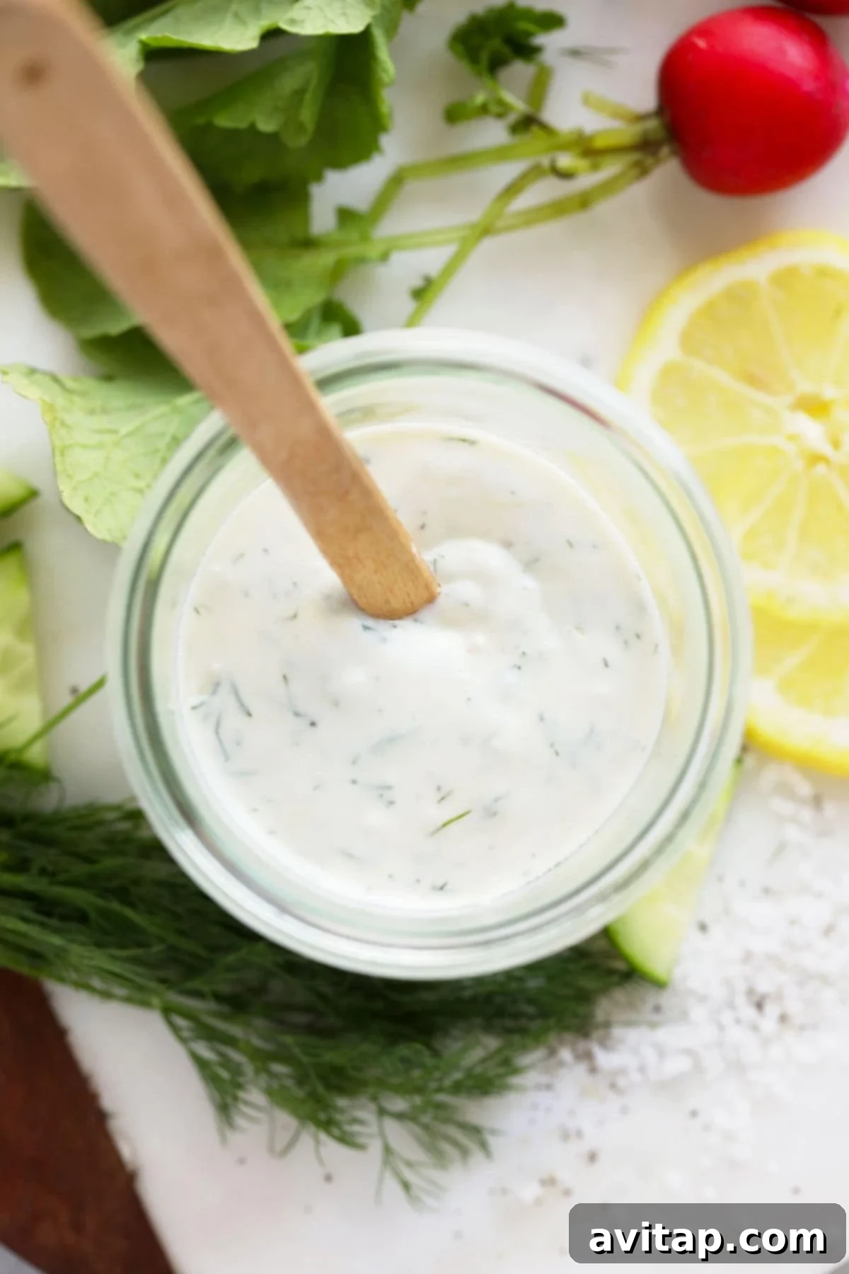 A Mason jar filled with healthy Greek yogurt dressing, featuring a decorative green label and fresh dill sprigs.