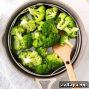 a person is slicing broccoli in a pan with a wooden spoon.