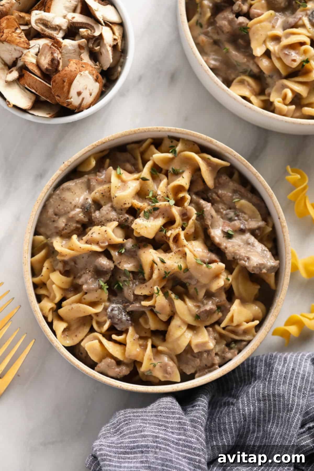 Effortless Creamy Beef Stroganoff 2 Beef stroganoff served generously over a bed of golden egg noodles in a rustic bowl.