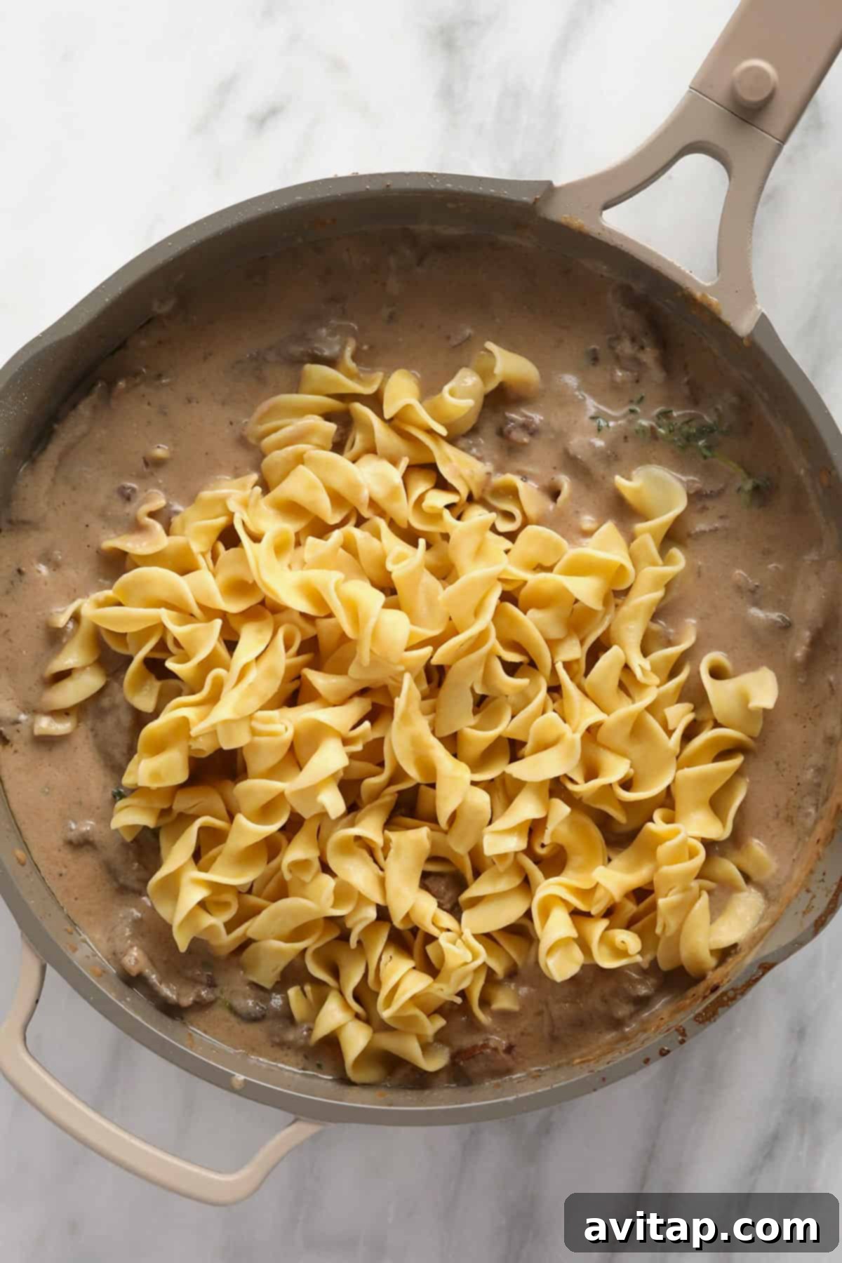 Effortless Creamy Beef Stroganoff 5 Classic beef stroganoff with egg noodles, simmering deliciously in a large pan.