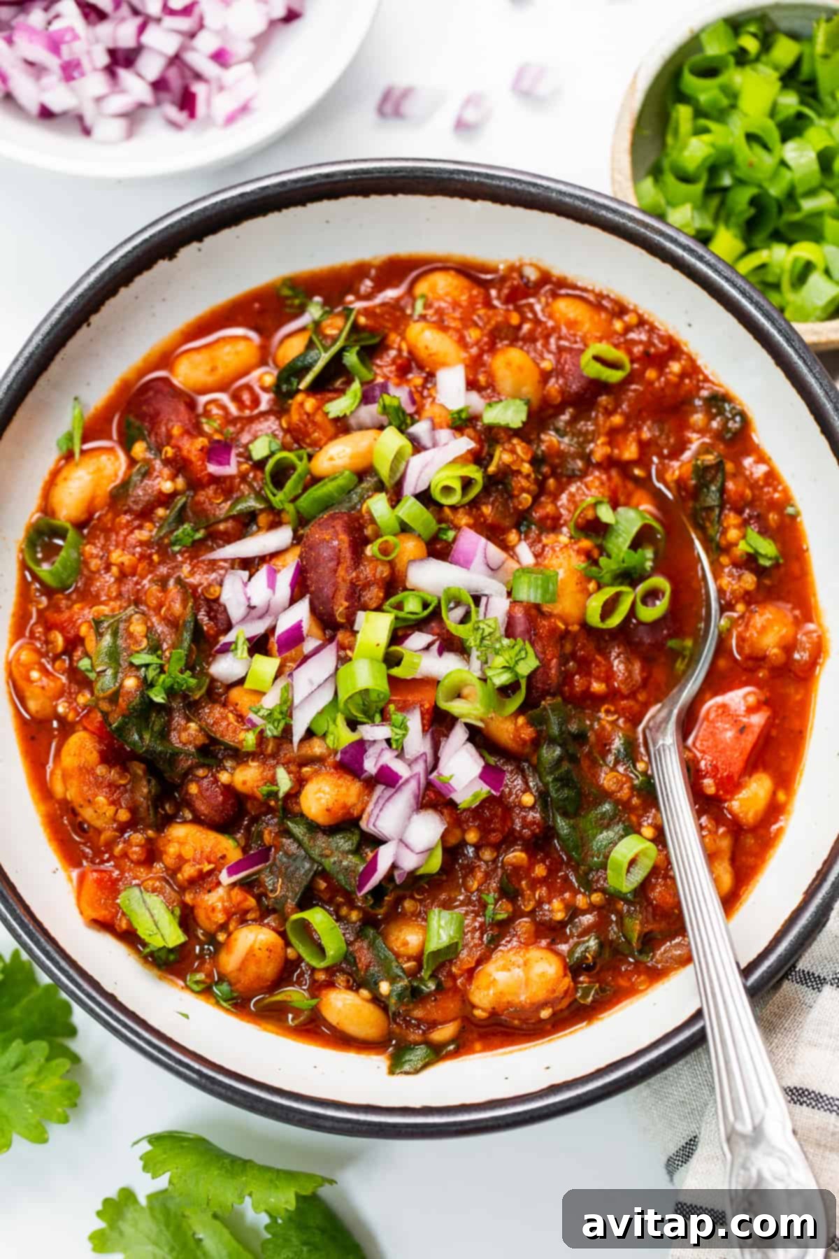 A vibrant bowl of roasted red pepper quinoa chili, garnished with fresh cilantro and a dollop of plant-based sour cream.