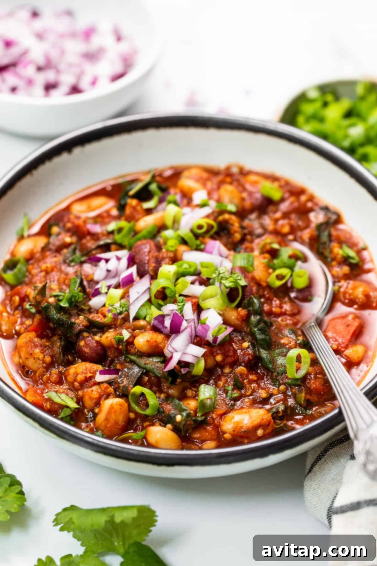A comforting bowl of roasted red pepper quinoa chili, garnished with fresh herbs and a drizzle of plant-based cream.