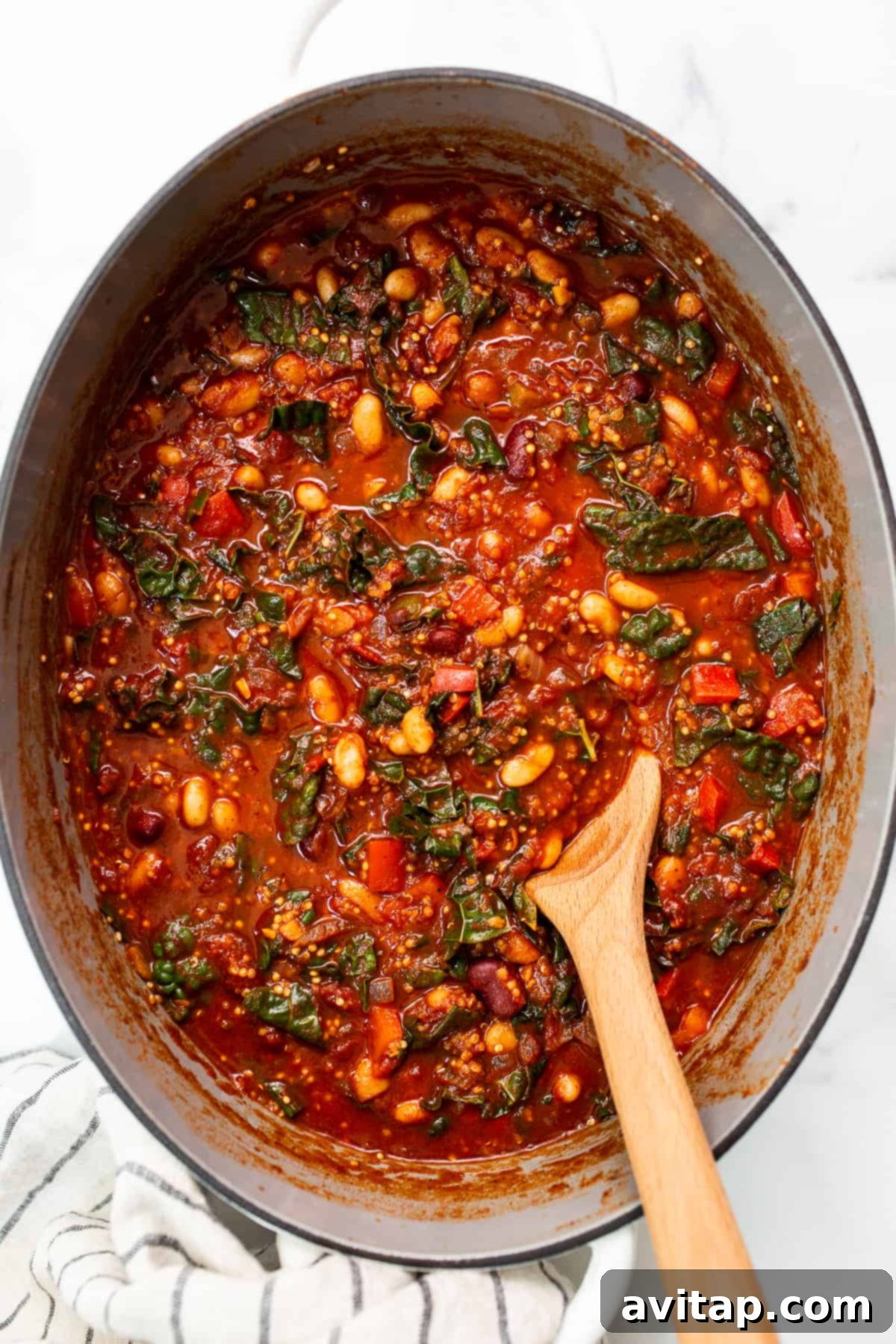 A close-up shot of rich quinoa chili bubbling gently in a large Dutch oven, with steam rising and vibrant colors of the ingredients visible.