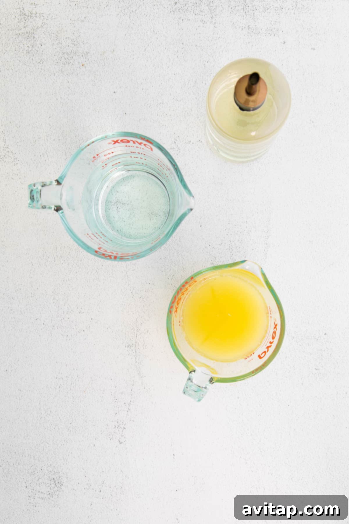 The three essential ingredients for homemade lemonade laid out on a countertop: a bowl of fresh lemon juice, a pitcher of water, and a jar of homemade simple syrup.