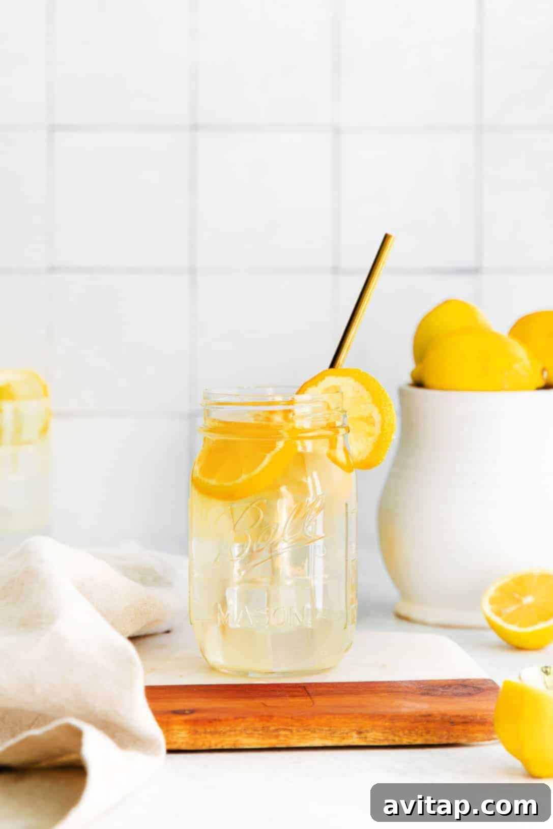 A charming mason jar filled with bright homemade lemonade, complete with a refreshing straw and elegant lemon slices.