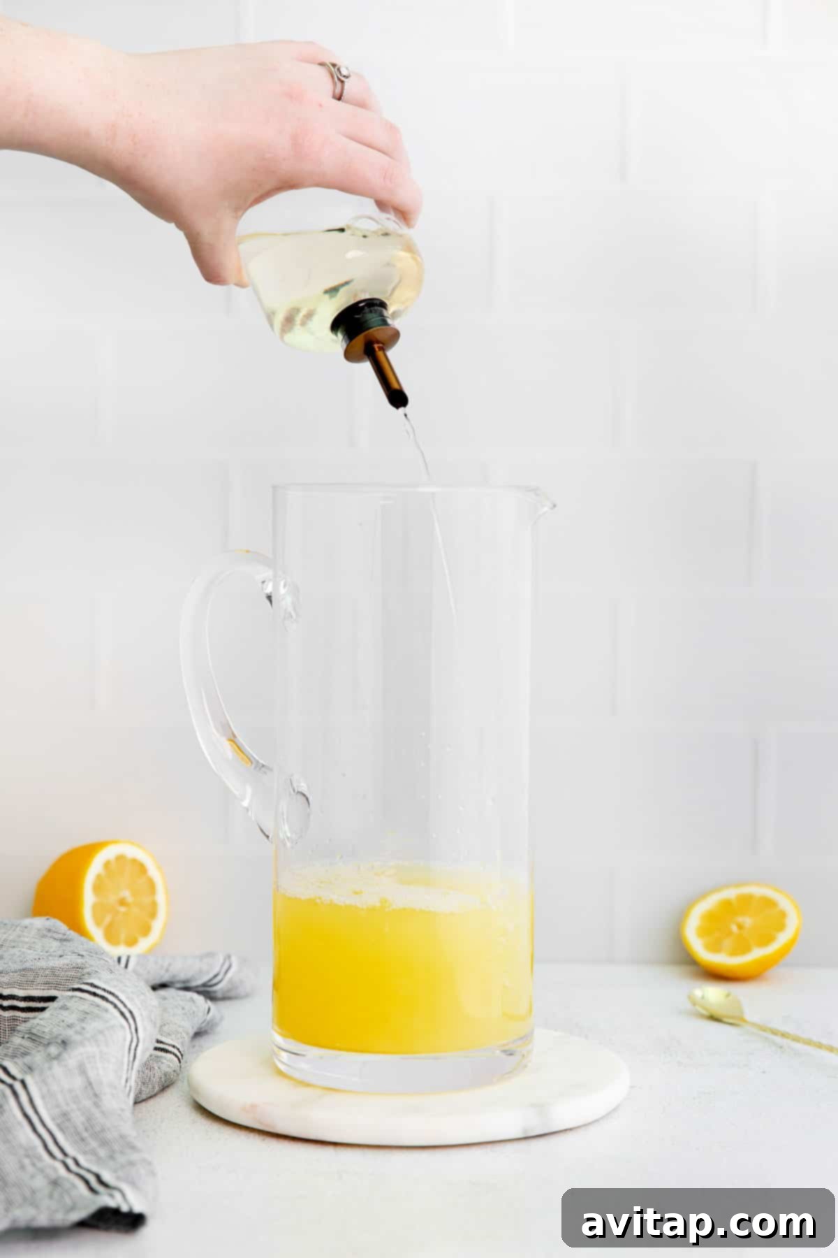 A stream of golden simple syrup being poured into a pitcher, mixing with lemon juice and water to create homemade lemonade.
