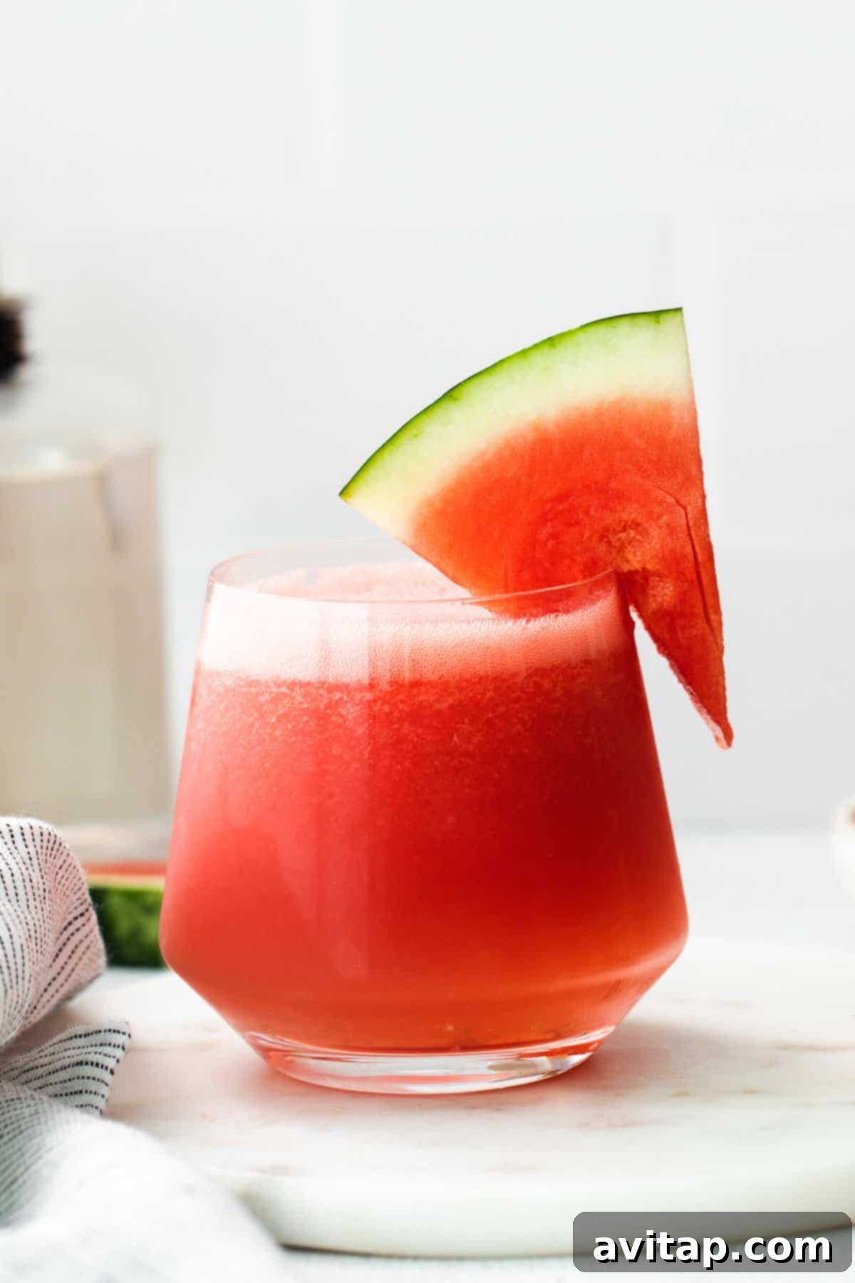 A vibrant pink watermelon frosé slushie in a glass, elegantly garnished with a fresh slice of watermelon.