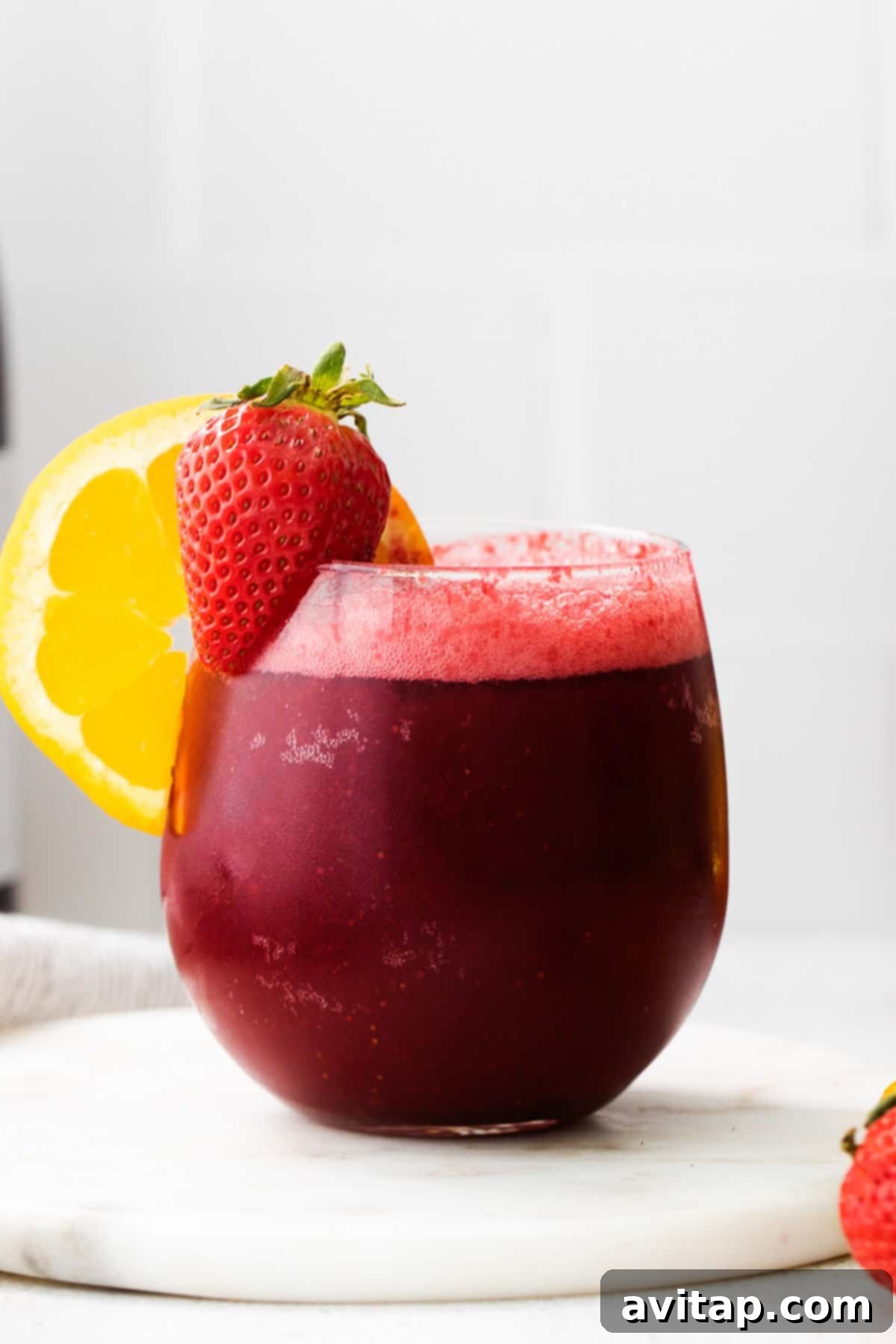 A rich red sangria wine slushie in a glass, adorned with a fresh lemon slice and ready to be enjoyed.
