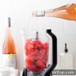 Pouring rosé wine into a blender with frozen fruit for a slushie.