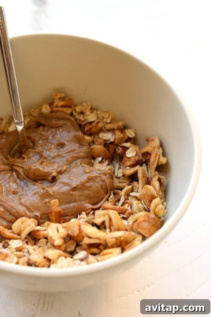 A vibrant, top-down view of all the wholesome ingredients for Apple Chai Energy Balls laid out in a large mixing bowl, ready for combination. Ingredients include rolled oats, dried apples, almond butter, and spices.