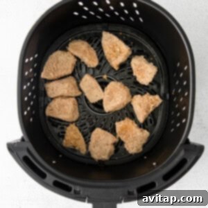 An air fryer basket filled with raw, breaded chicken nuggets, carefully arranged in a single layer to avoid overcrowding, ready for cooking.