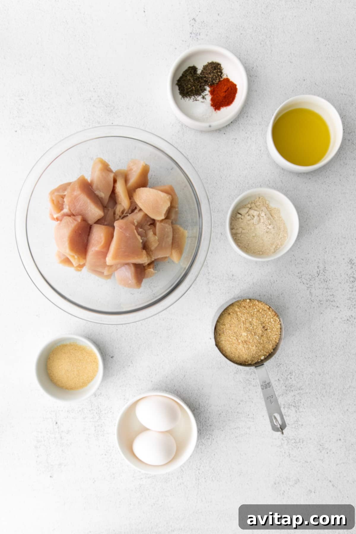 A colorful array of ingredients for air fryer chicken nuggets, including chicken breast, breadcrumbs, eggs, olive oil, and various spices, neatly laid out on a kitchen counter, ready for preparation.