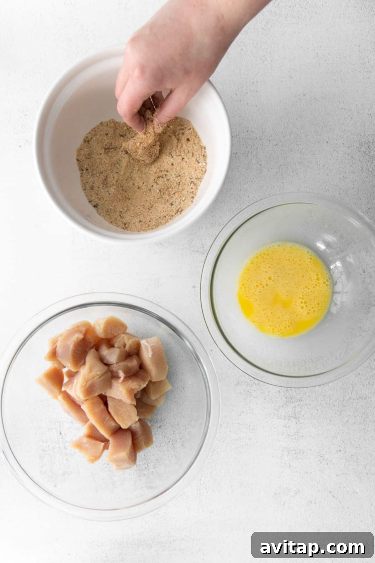 A close-up shot of chicken pieces being dipped into a bowl of seasoned breadcrumbs, ensuring an even and thorough coating for perfect air frying results.