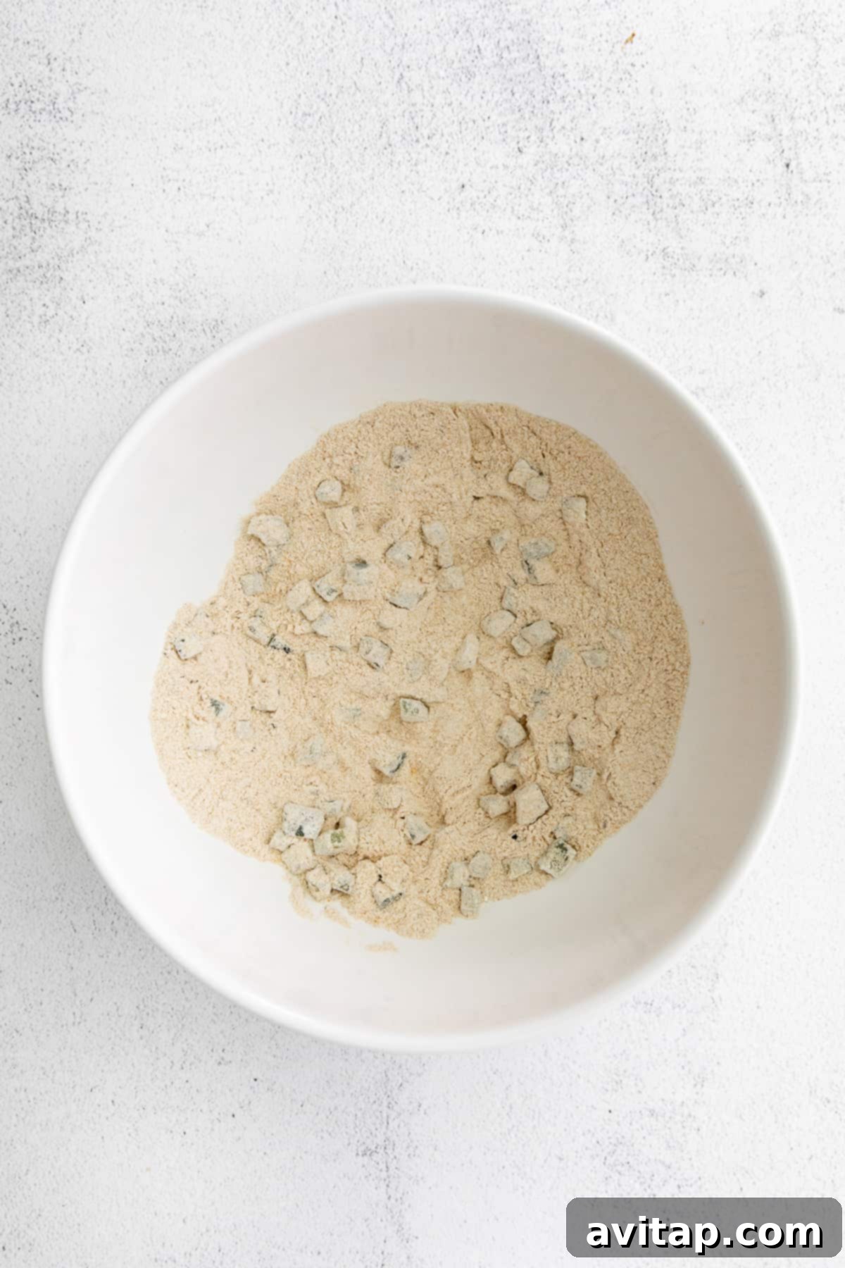A bowl of vibrant corn fritter batter, showing whole corn kernels, green chives, and pieces of red pickled jalapenos mixed together, ready for cooking.