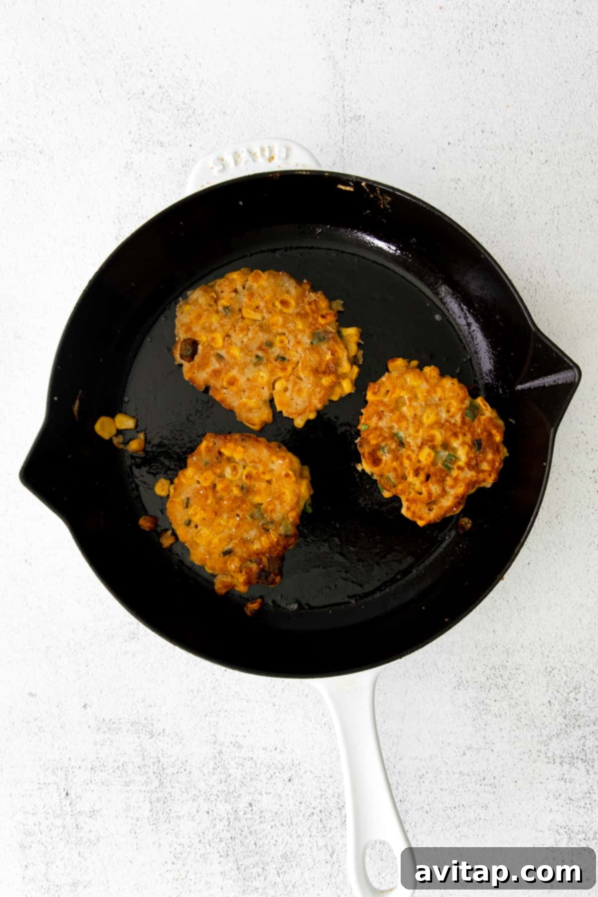 Several crispy corn fritters cooking in a large cast iron pan, showing their golden-brown color and inviting texture.