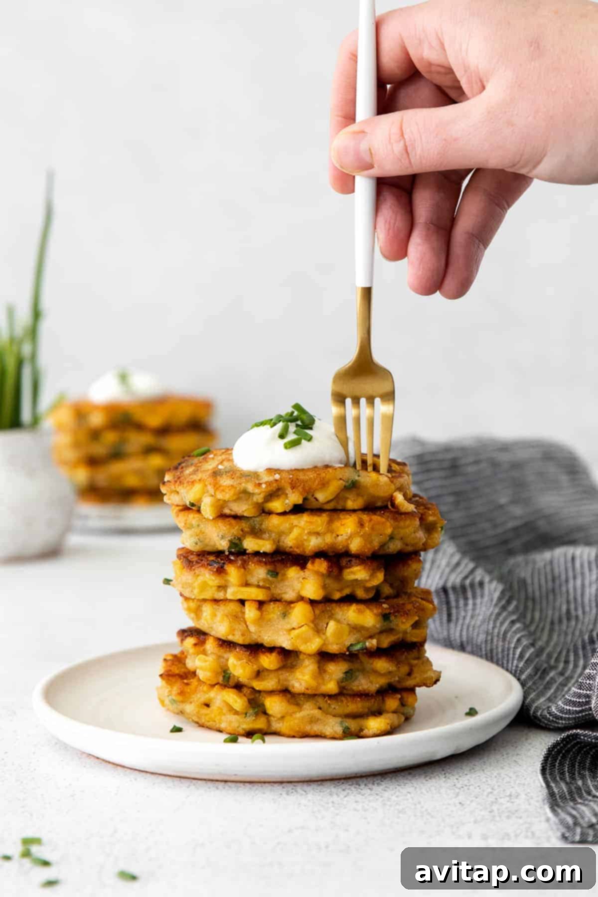 A perfectly stacked tower of crispy corn fritters, generously topped with creamy Greek yogurt and freshly sprinkled chives, ready to be enjoyed.