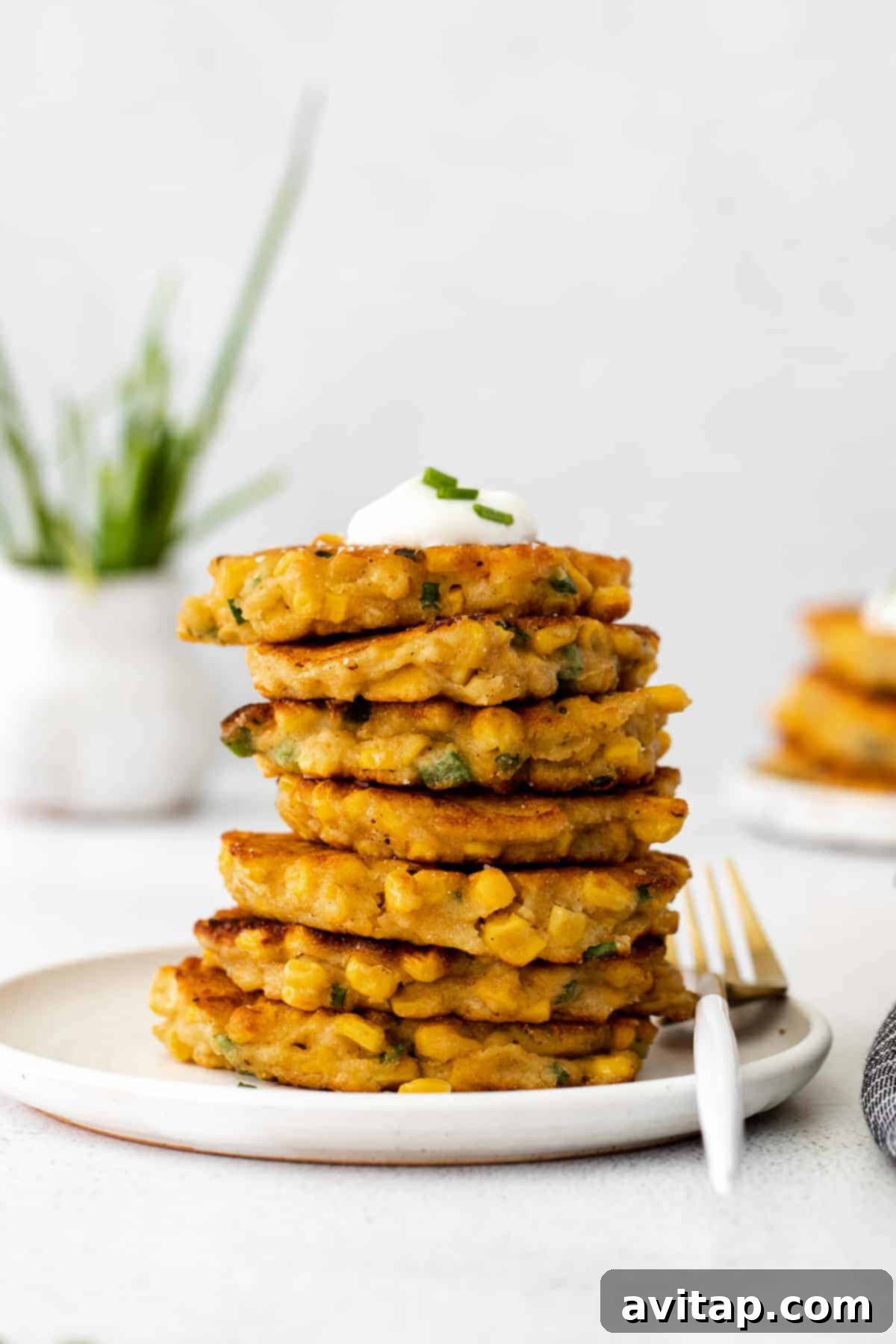 A close-up of a single corn fritter topped with a swirl of Greek yogurt, showcasing the texture of the corn kernels and the vibrant chives. 