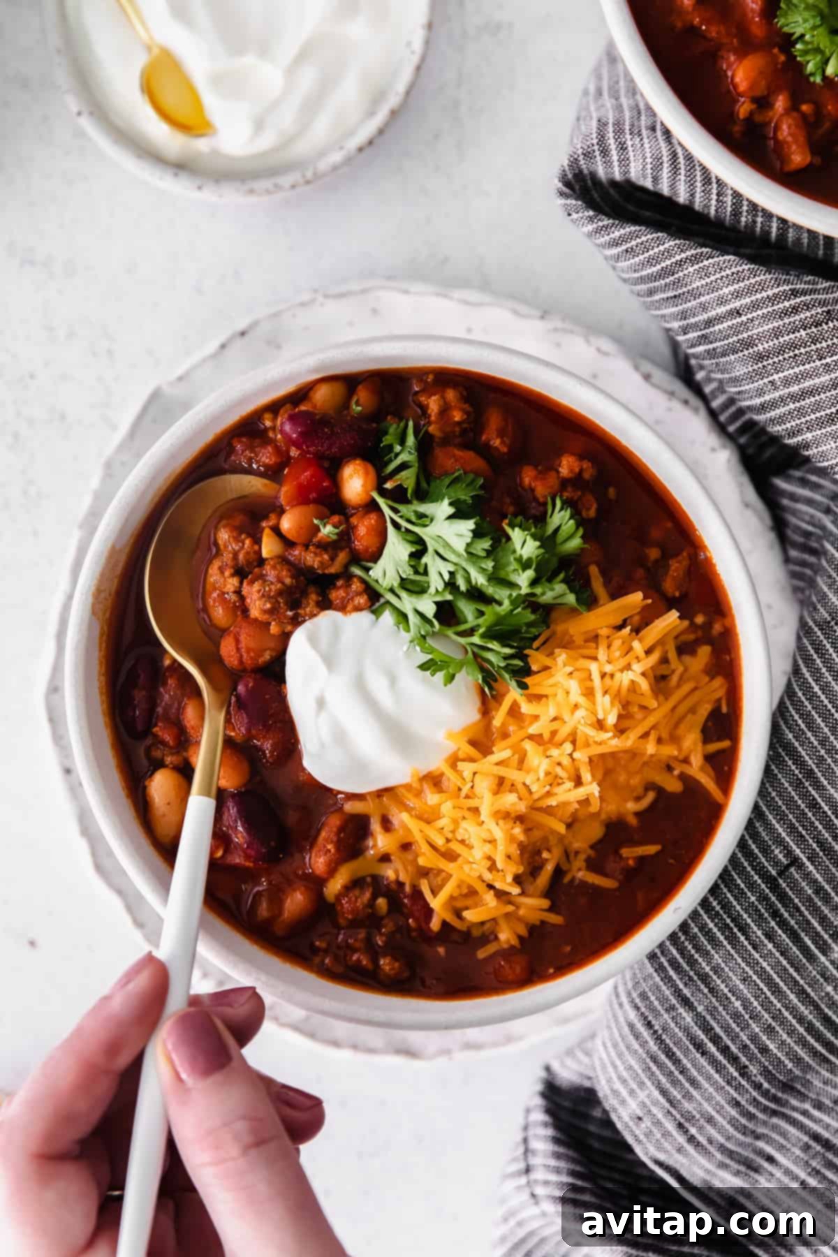 Whip up a batch of this delicious Instant Pot Chili in no time! This Instant Pot Chili recipe is made with ground beef, beans, tomato products, and homemade chili seasoning. Instant Pot chili in a bowl, generously topped with shredded cheese, Greek yogurt, and fresh parsley, ready to be enjoyed.
