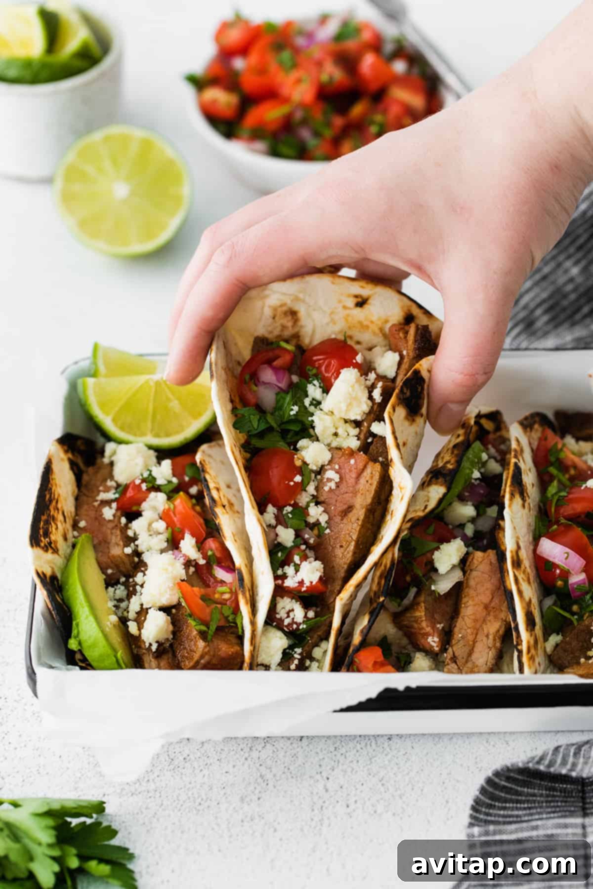 hand grabbing a steak taco from a platter of steak tacos