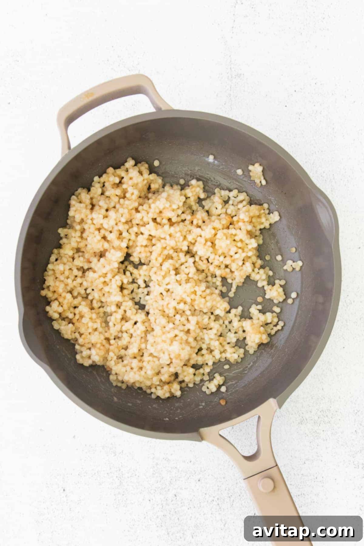Israeli couscous being toasted in a pan with olive oil and lemon juice