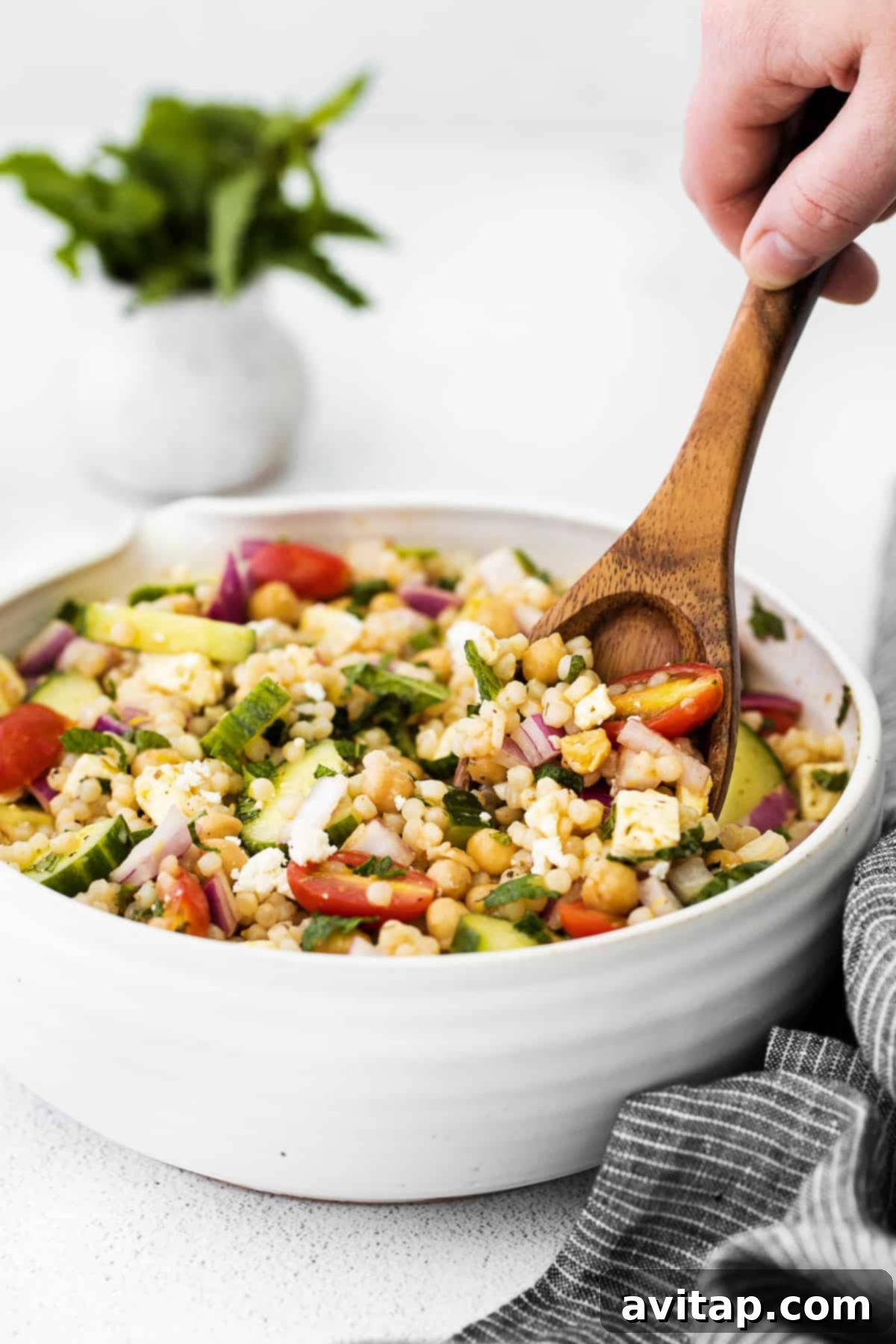 Mediterranean couscous salad being mixed in a large bowl with a spoon