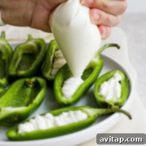 A person piping cream cheese mixture into halved green peppers.