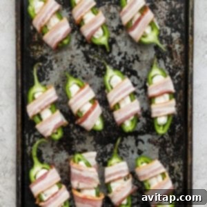 Bacon-wrapped peppers arranged neatly on a baking sheet.