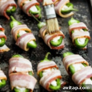 Maple syrup being brushed over bacon-wrapped jalapenos on a baking sheet.