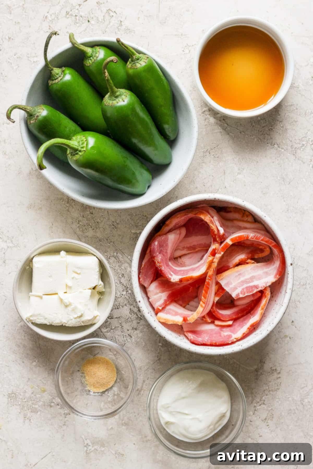 A collection of ingredients laid out on a table, including fresh jalapenos, cream cheese, bacon, and maple syrup.