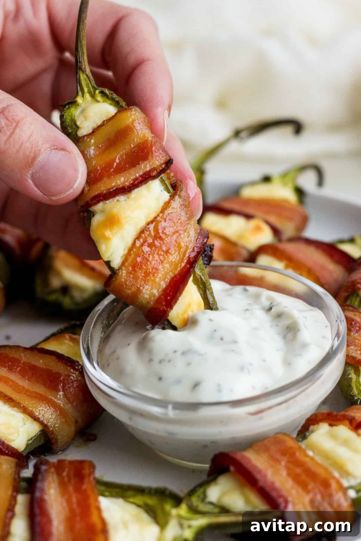 Bacon wrapped jalapenos arranged on a platter with a small bowl of dipping sauce.